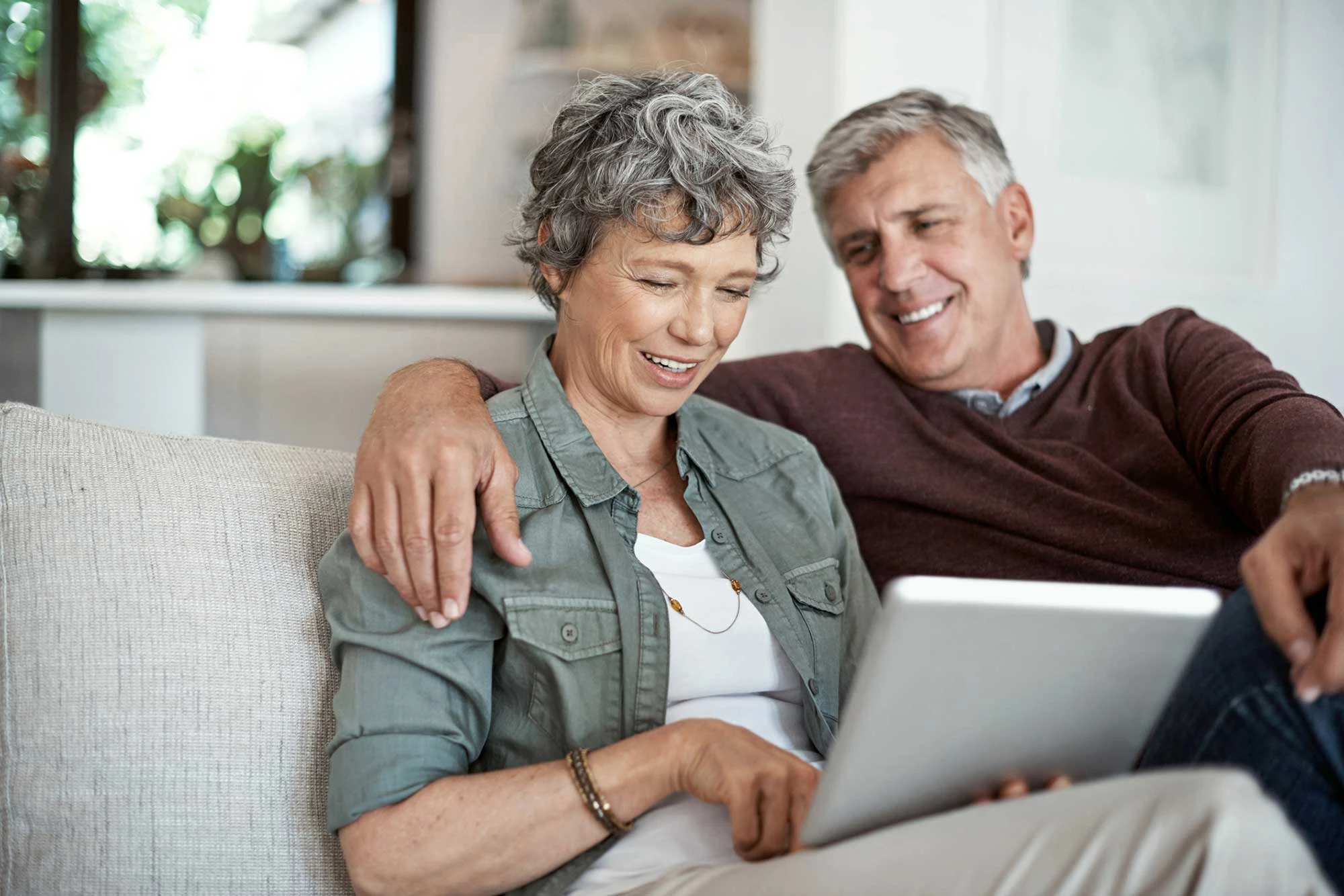 Senior couple relaxing on couch looking at tablet at Cypress Senior Apartments